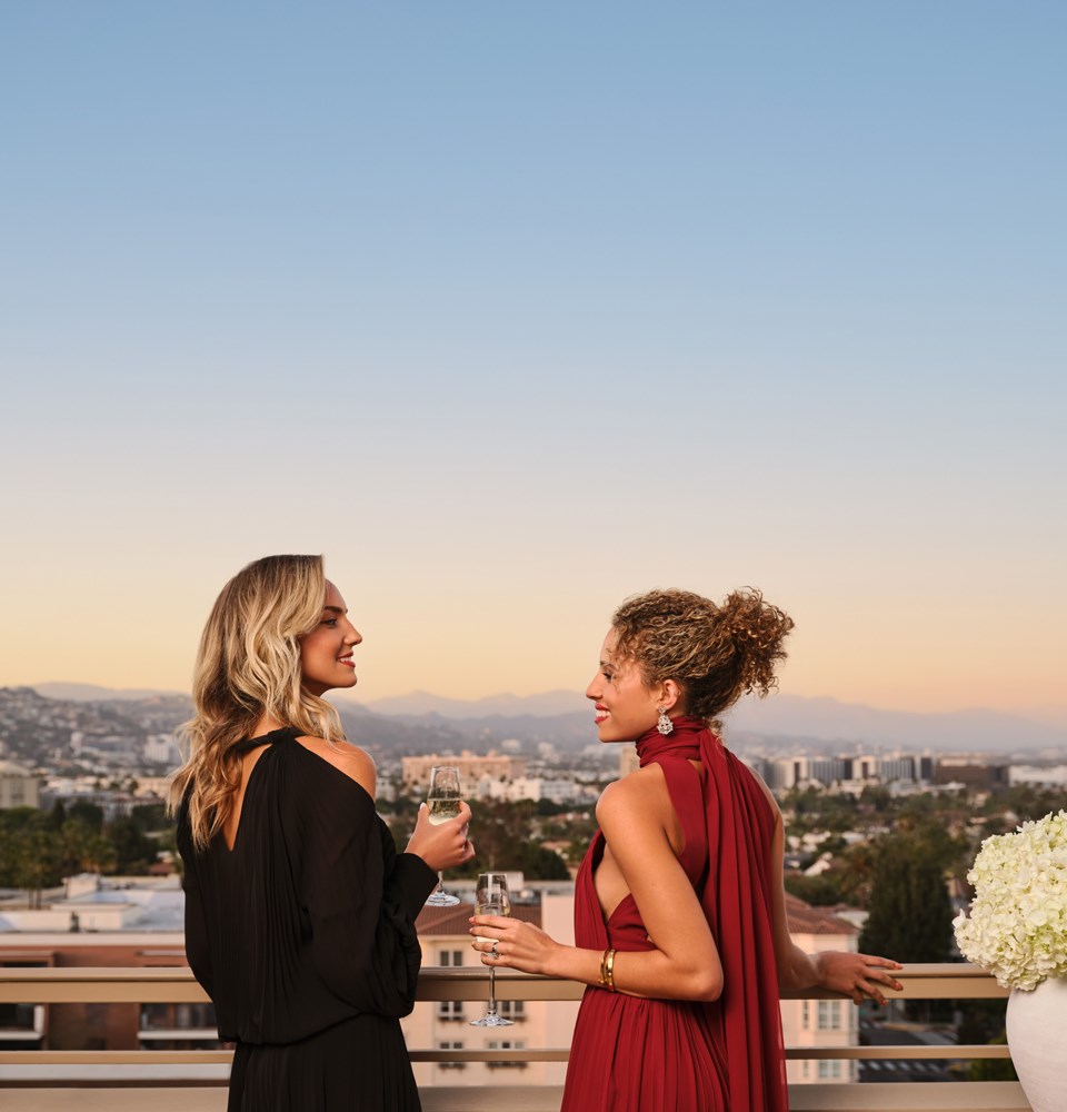 Two women sipping champagne on an outdoor balcony overlooking Beverly Hills during sunset