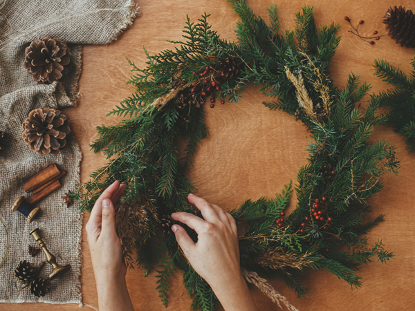 a woman's hands decorating a wreath with supplies all around