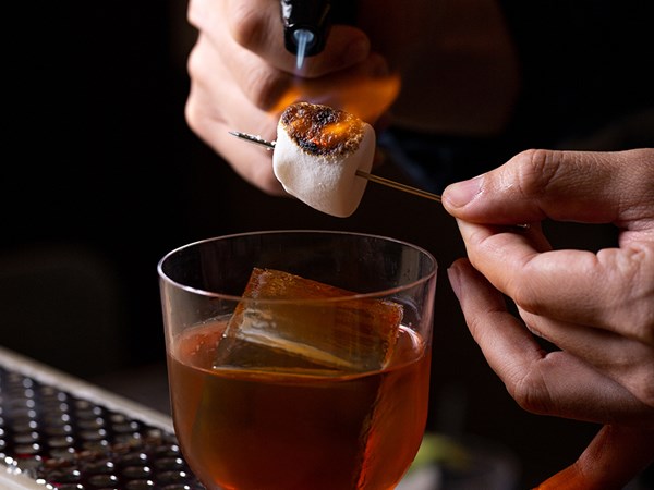 Head mixologist lighting flame to embellish cocktail