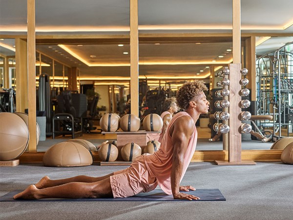 Man in pink gym clothing performing up dog pose on yoga mat in hotel gym