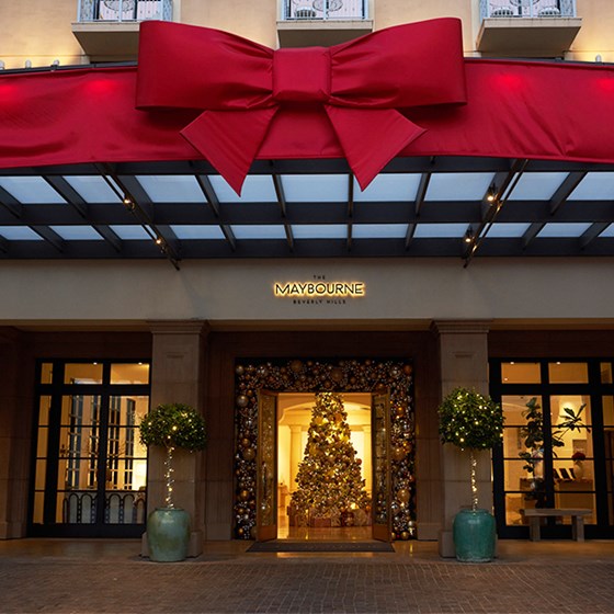 Giant red bow decorating The Maybourne Beverly Hills' entrance with open doors showing Christmas tree