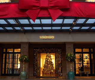 Giant red bow decorating The Maybourne Beverly Hills' entrance with open doors showing Christmas tree