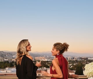 Two joyful women chat, exchanging smiles and champagne, in lively and animated conversation.