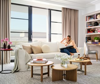 A lady rests near a wide window in her cozy living room, reclining on her sofa.