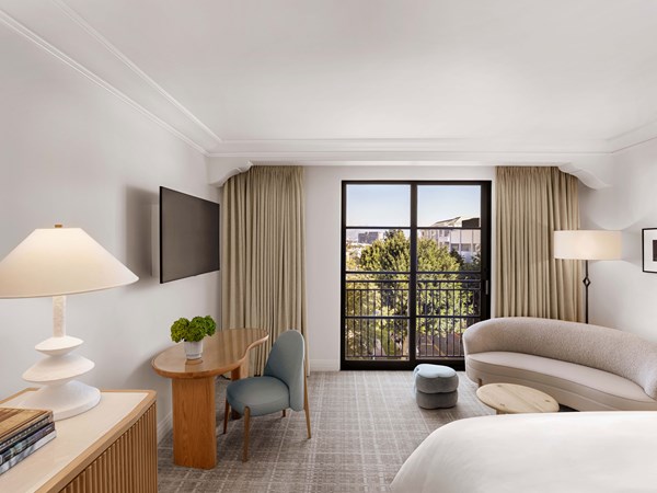 Hotel room with television mounted on the wall, dresser, desk, sofa and bed, with sliding glass doors leading to a juliet balcony