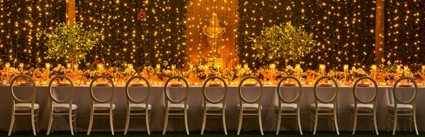 Long table and chairs set up for an evening event with fairylights hanging behind