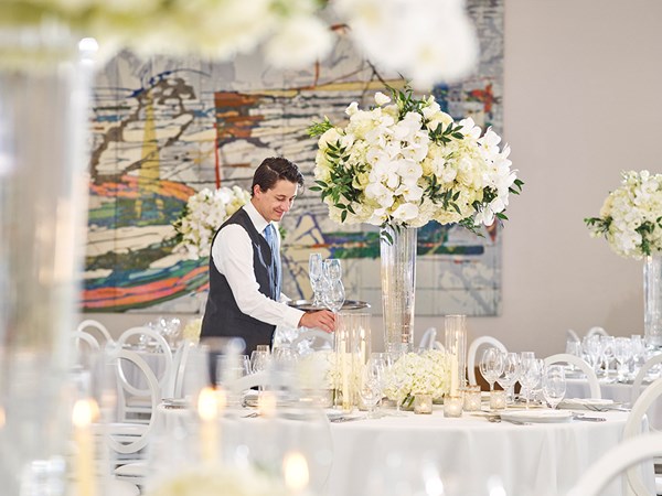 Waiter setting up plates and glasses around candles on a table at a wedding