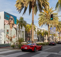 Red sports car driving down Rodeo Drive with palm trees and designer shops