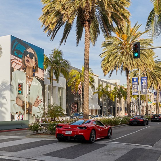 Red sports car driving down Rodeo Drive with palm trees and designer shops
