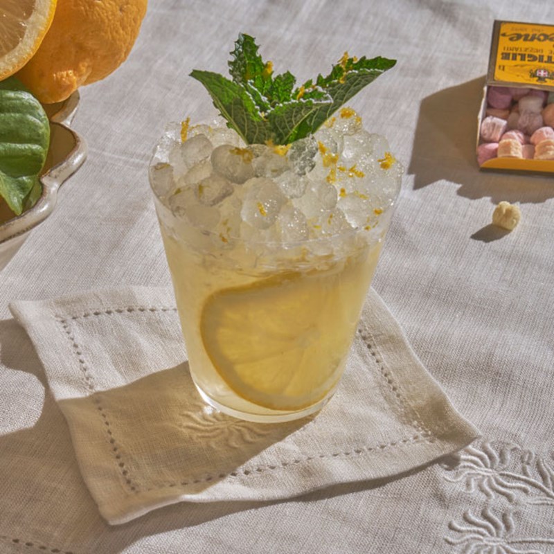 Short yellow cocktail with ice, a lemon slice and mint garnish