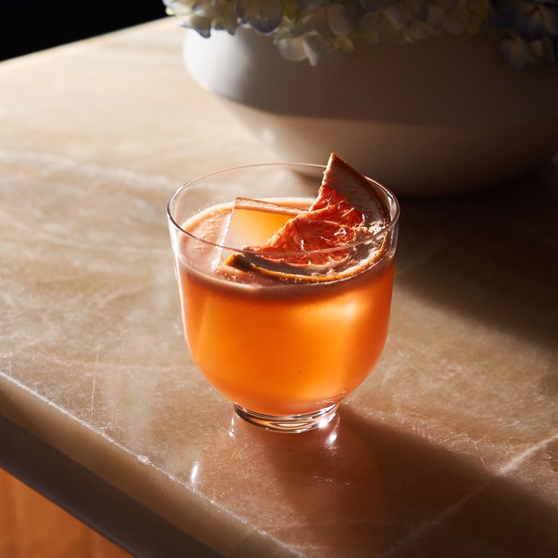 Orange colored cocktail with a dried orange slice garnish