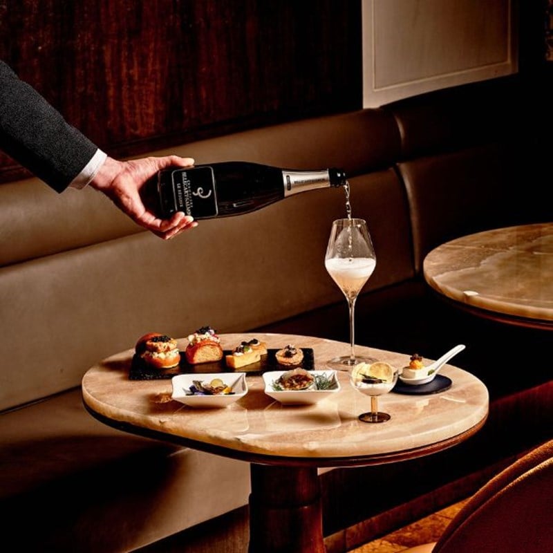a man's hand pouring champagne over a table fille with caviar tasting bites