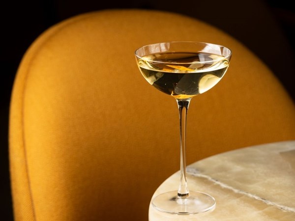 a martini in a skinny martini glass on a marble table in front a deep orange cushion chair