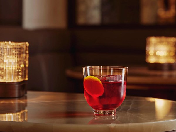 A cocktail with a large piece of ice and a leaf on a marble bar.