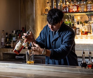 Bartender behind a bar pouring alcohol into a vessel