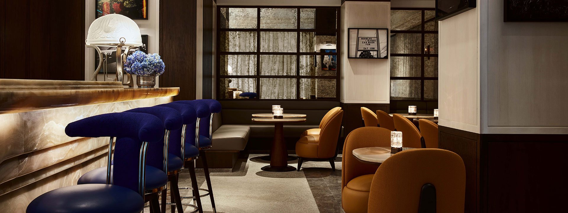 The seating area of The Maybourne Bar. On the left, there are 5 dark blue stools at the bar