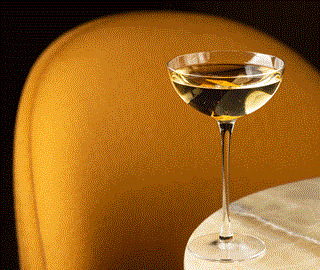 Cocktail in a martini glass on a table with a yellow chair back behind it