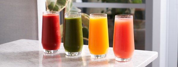 Four brightly colored juices in glasses on a marble table top