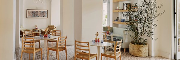 Café tables and chairs. The floor is covered in pink and white tiles. There's a large potted tree in the corner.