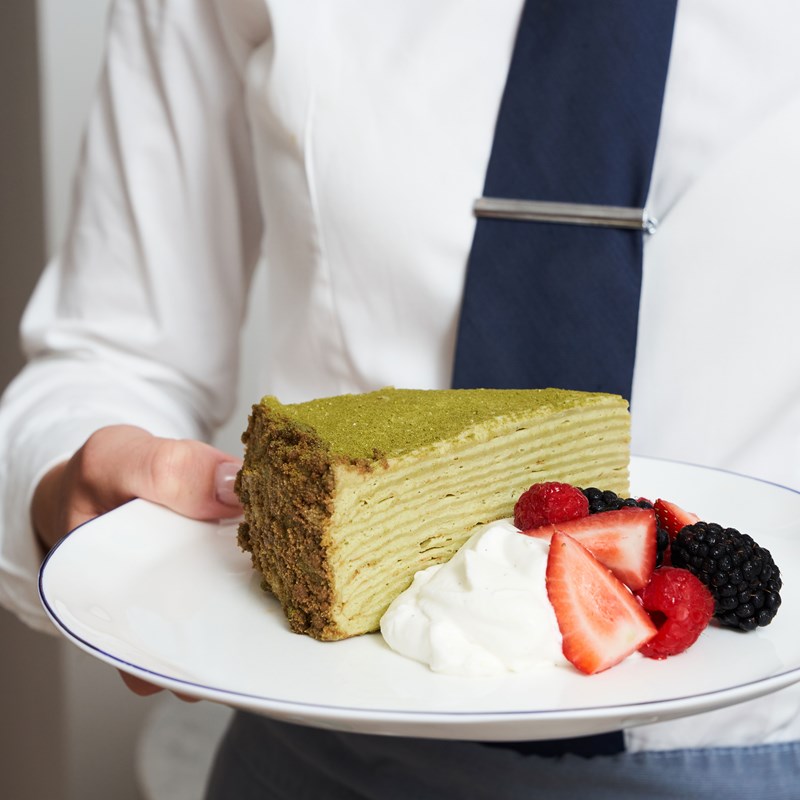Serve holding a plate with a slice of matcha crepe cake with berries and cream
