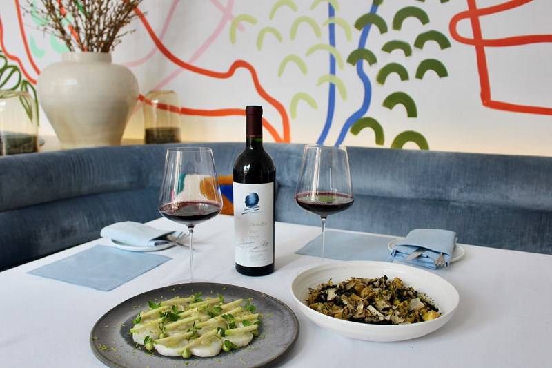 Booth in a restaurant with a bottle of Opus One wine, two wine glasses, a plate of pasta and a plate of scallops