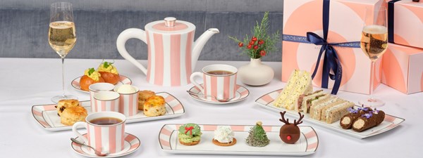 Festive afternoon tea with striped pink china, sandwiches, scones, holiday desserts, sparkling wine, and gift boxes in the background