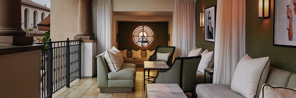 A terrace with olive colored outdoor seating and portrait photos hanging on the walls of people smoking cigars.