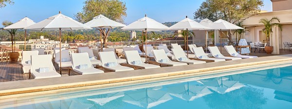 Rows of white sunbeds with parasols in front of the rooftop pool with a view over the L.A skyline