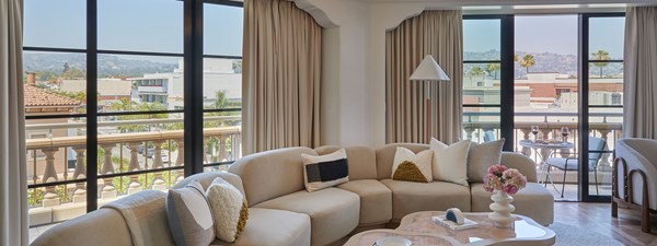 A large, curved beige couch in the living area of a hotel room. There's a sliding glass door to a balcony with a table and wine glasses.