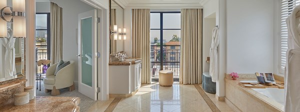 The bathroom of the California Suite hotel room showing a bathtub, a large vanity with a mirror, and tall windows letting in sunlight.