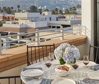 Hollywood Suite at The Maybourne Beverly Hills - table on the suite terrace with plates, wine glasses, bread and flowers placed on the table and view onto Beverly Hills