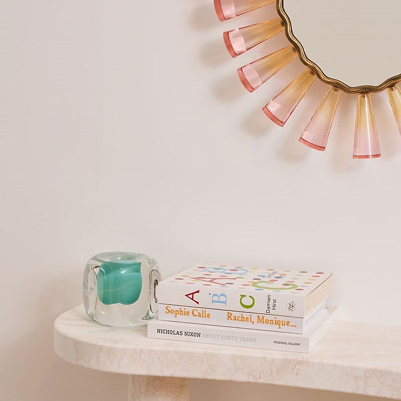 White and curved marble table with coffee table books on top and the edge of a pink mirror above