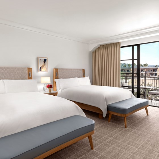 Two queen beds in a hotel room. There is a garden table and two chairs outside on a private balcony.