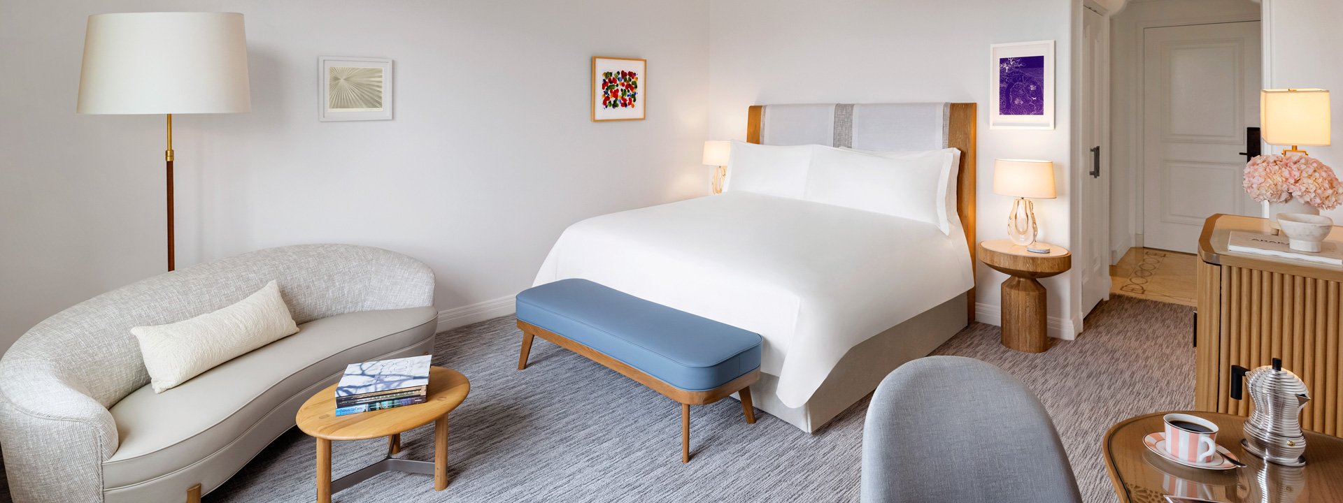 A king sized bed in a hotel room. There's a curved couch and a small wooden table with books.