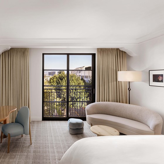 The living area of The Maybourne Room at the Maybourne Beverly Hills hotel. There is a large window with a tree outside letting in light.