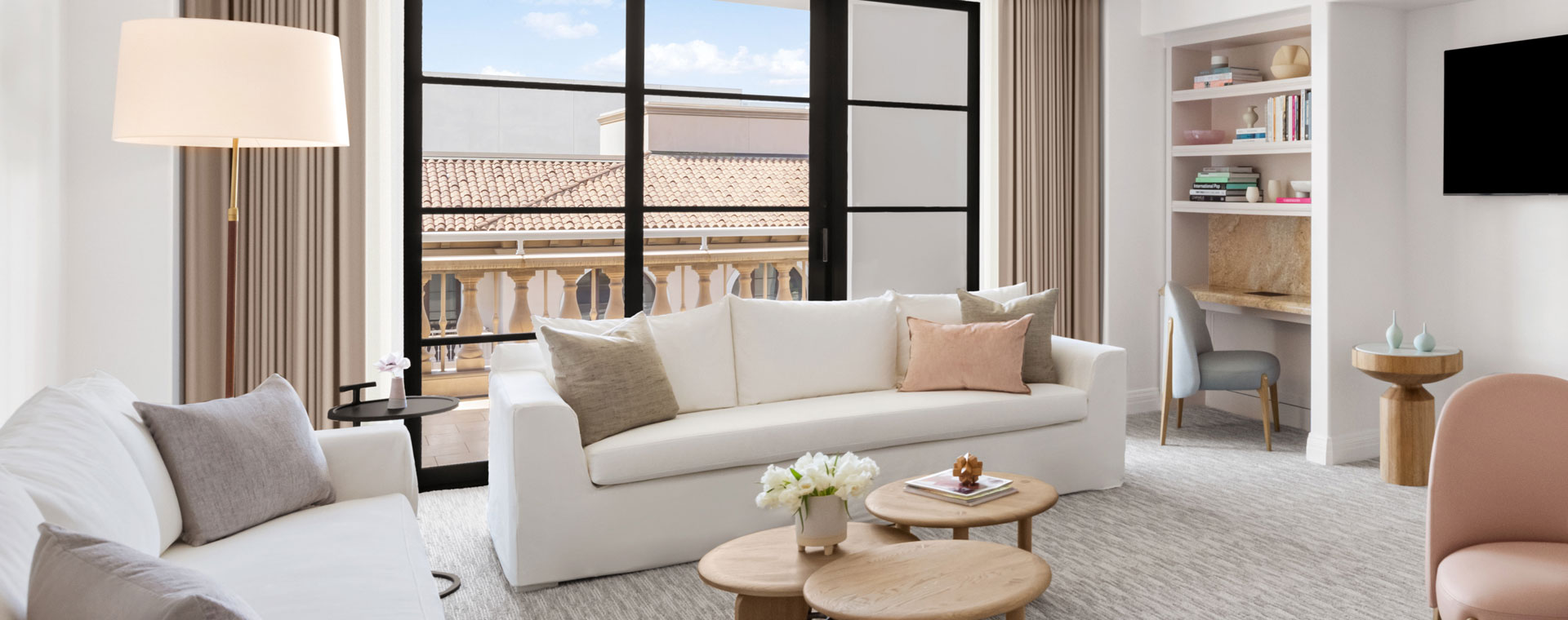 The living space of a hotel suite. There is a white couch and love seat in front of a large sliding glass door that leads to a terrace.