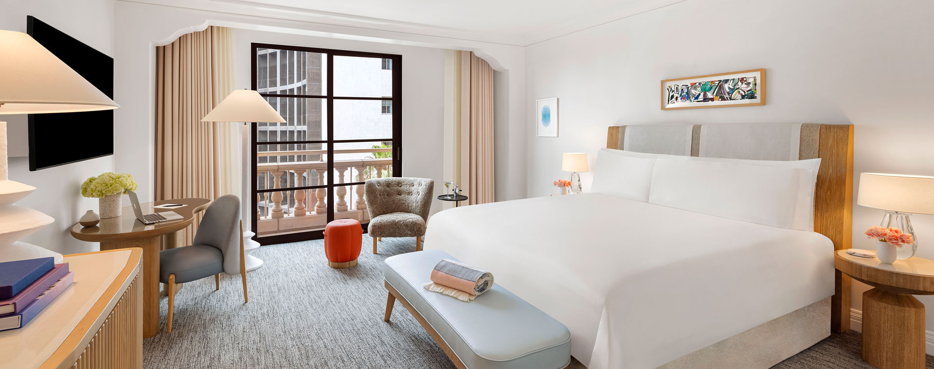 A king sized bed in a hotel room. There is a wall-mounted tv and a large window that lets in sunlight.