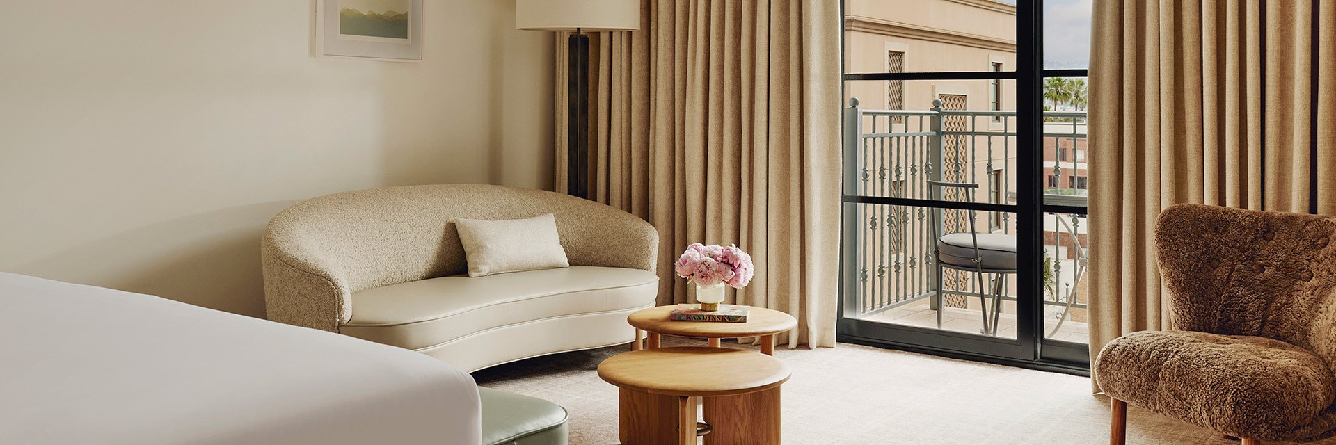 A hotel living area with a sofa and a wooden coffee table with pink flowers. There's a sliding glass door to a balcony.