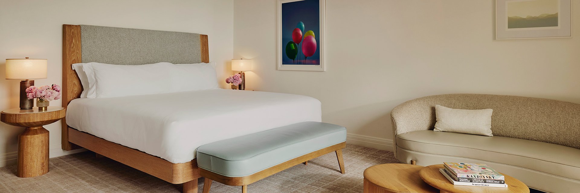 A neat king's sized bed with white sheets, two wooden nightstands with pink flowers and lamps, a coffee table, and a sofa.