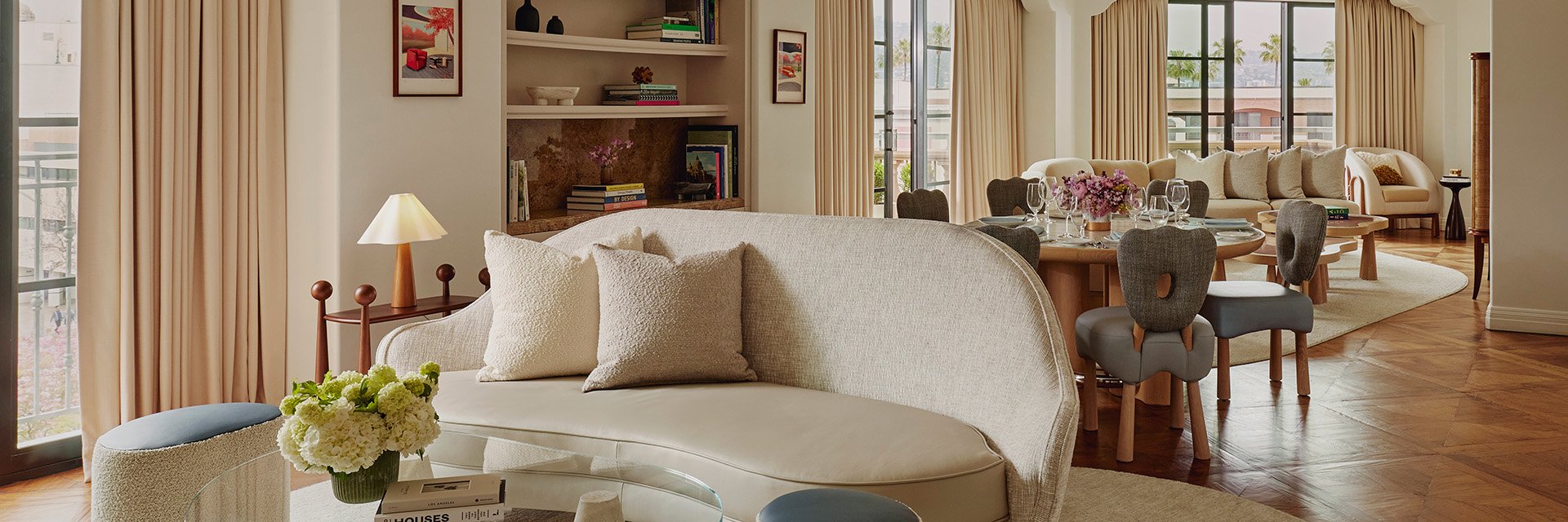 Behind a curved sofa and a glass table is a dining table with six chairs. There's another living space with couch and chair.