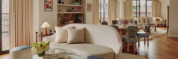 Behind a curved sofa and a glass table is a dining table with six chairs. There's another living space with couch and chair.