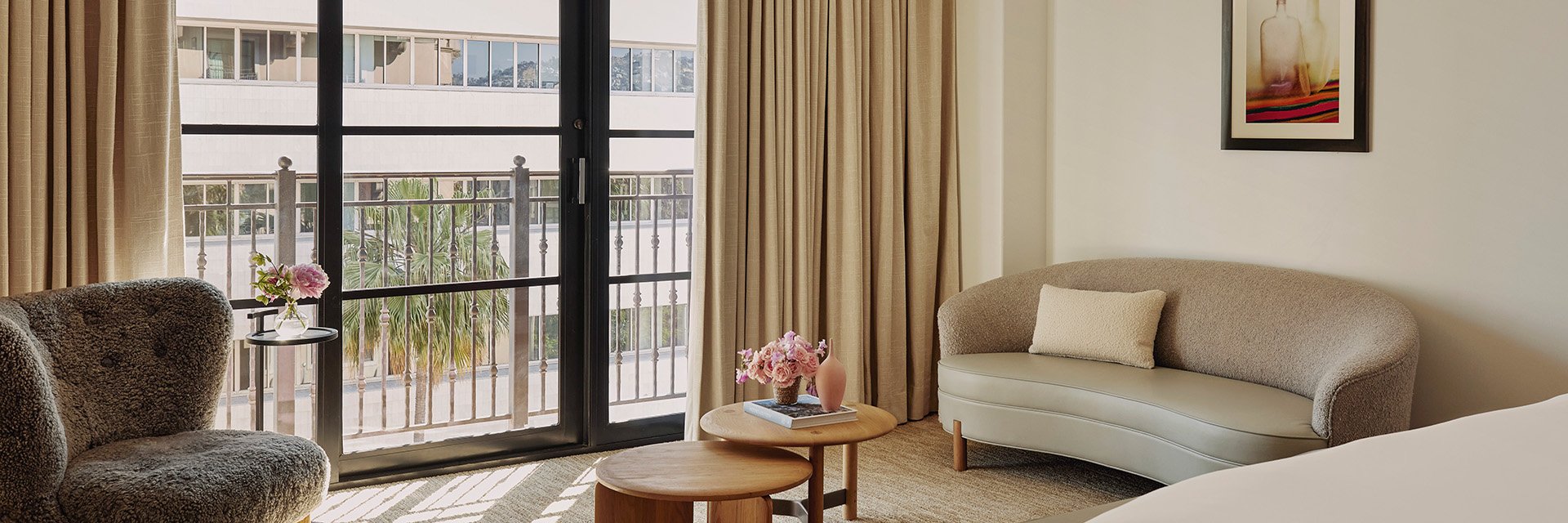 A curved ivory couch in front of sliding glass doors. A wooden coffee table with potted pink roses. A plush, sitting chair.