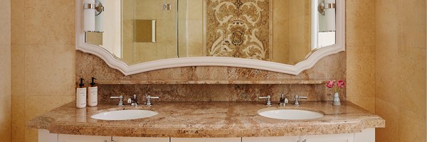 A brown marble sink top with white drawers. In the mirror a shower can be seen with a tiled mosaic wall.