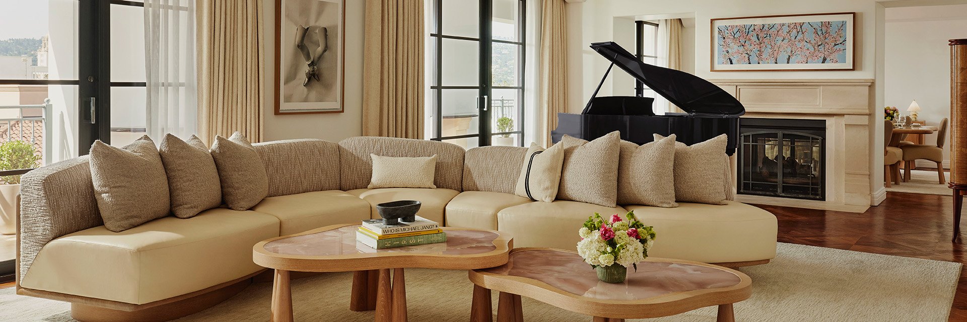Large L-shaped beige sofa with beige cushions in the living area of suite. A large, blue grand piano sits by a fireplace.