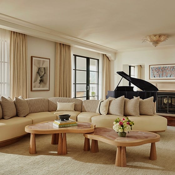 Large L-shaped beige sofa with beige cushions in the living area of suite. A large, blue grand piano sits by a fireplace.