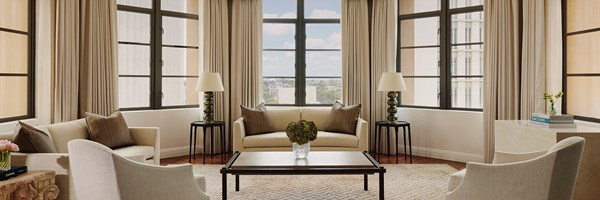A hexagon shaped living room with white couches and sitting chairs. The walls are large, floor to ceiling windows.