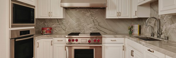 A kitchen with marble countertops, a sink, a modern stove, oven, microwave, and white drawers. The stove has red knobs.