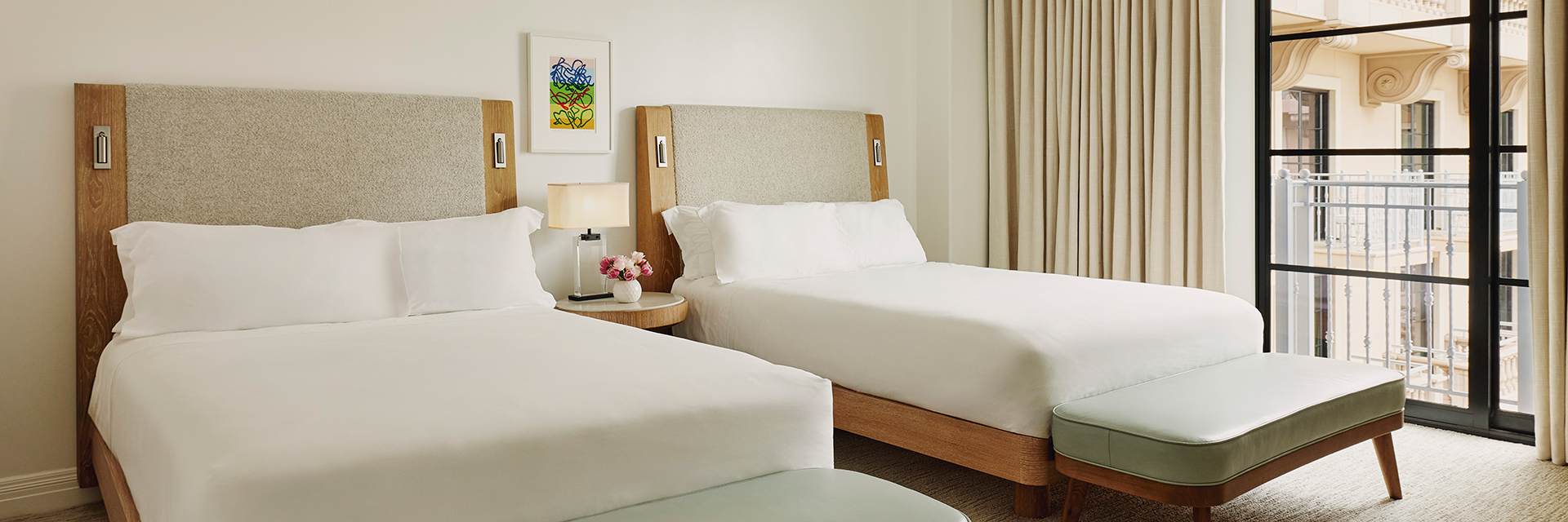 Neat bedroom with two beds, night lamp on a side table; well-organized and inviting with pink and violet roses in a vase.