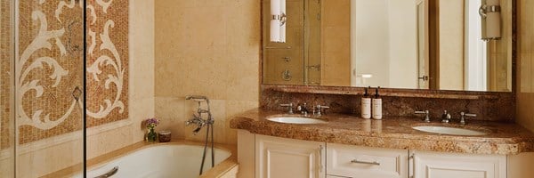 A tiled bathroom, a bathtub with a tiled wall mosaic, and a brown marble sink with white drawers.