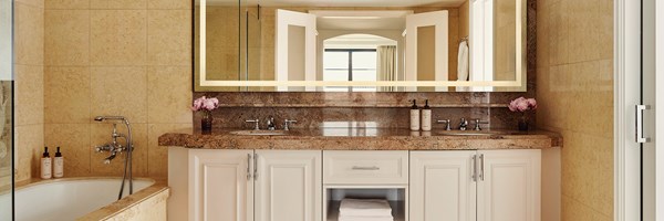 A brown marble sink top with white drawers and a bath tub. There are pink potted flowers on the sink.
